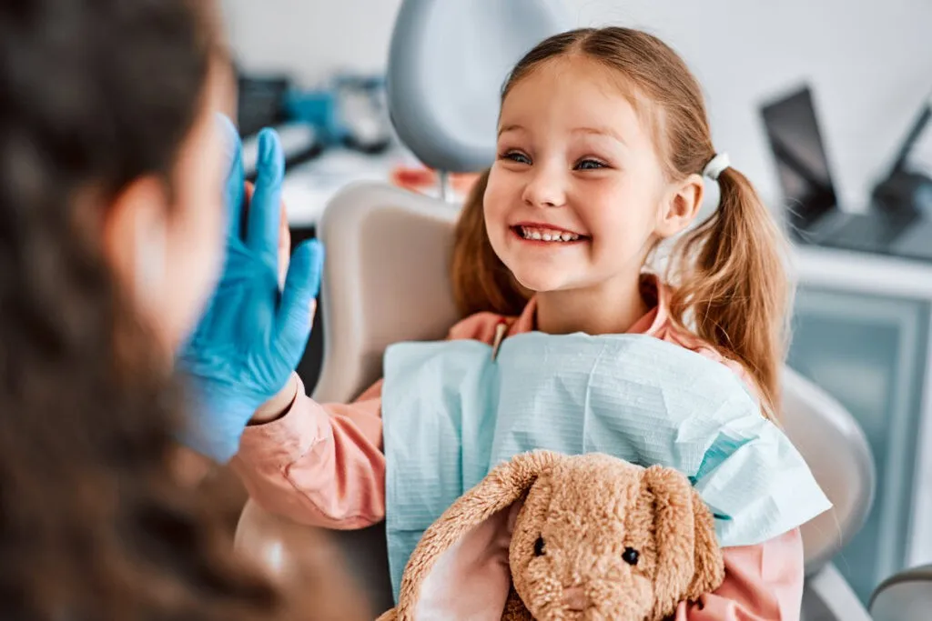 At the doctor's appointment. A candid emotional photo of a child sitting in a dental chair, holding a toy rabbit and cheerfully giving a high-five to the nurse.