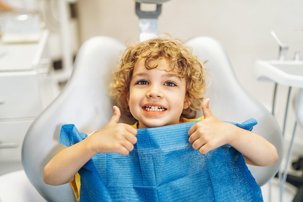 Happy cute little boy in dental ofiice showing thumbs up after treatment