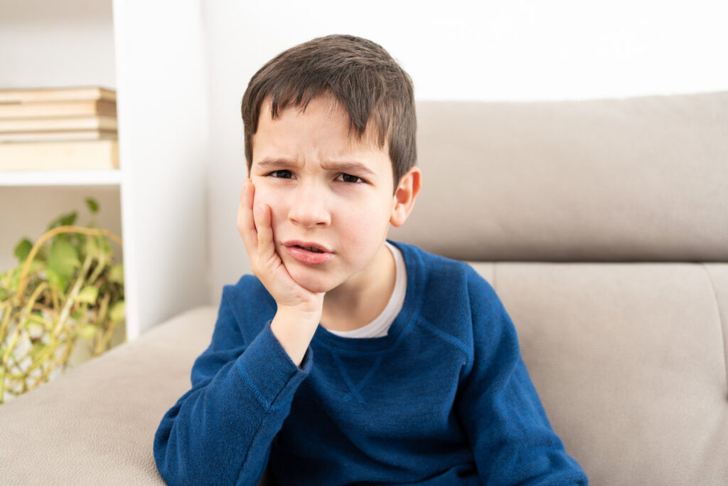 Stressed child complaining suffering toothache sitting on a couch at home