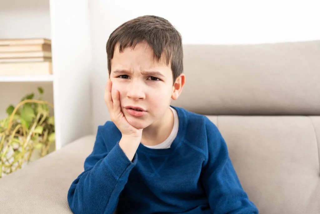 Stressed child complaining suffering toothache sitting on a couch at home