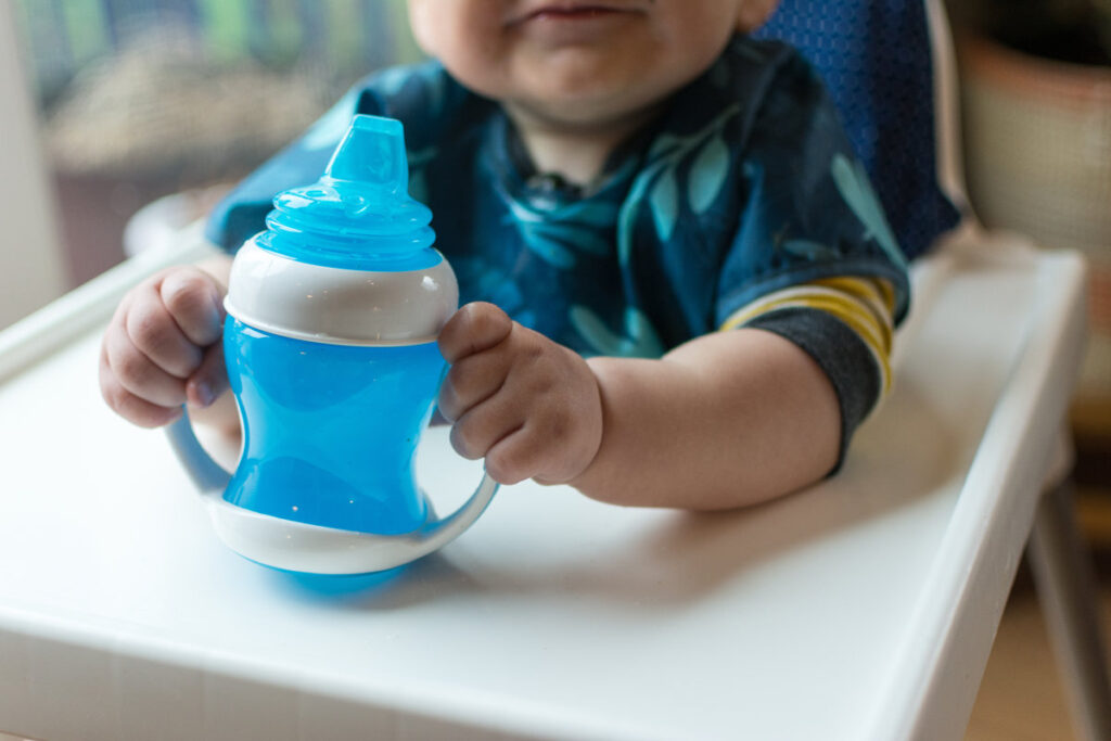 Toddler grasping handles of a sippy cup; learning to use a cup to drink water